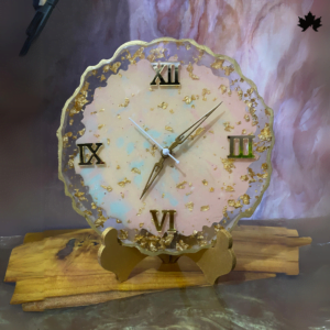 Alt text for the image: Blush Elegance Designer Table Clock by Fankaarlok, featuring a golden base supporting a round clock face with pastel pink and white hues, adorned with Roman numerals and gold flakes, positioned on a wood stand.