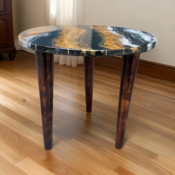 Elegant round table with a high-gloss top featuring rich blue and gold marbling effects that create a luxurious look. The Artisan Centerpiece table stands on three dark stained wooden legs that taper gracefully, complementing the sophisticated top. Set in a room with hardwood flooring and natural light, this table blends modern design with classic elegance, ideal for enhancing any contemporary home setting.