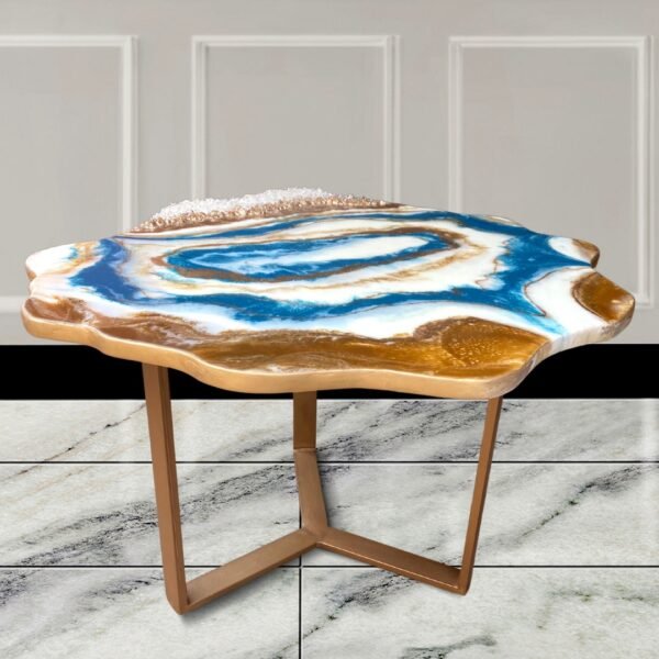 Luxurious handcrafted center table featuring an irregularly shaped top with swirling patterns of blue, white, and gold resin, resembling aerial views of a coastal landscape. The table is supported by a sleek bronze-colored metal base, adding a modern touch to the organically flowing design. This striking table combines functionality with artistic beauty, making it a standout piece in any contemporary interior.