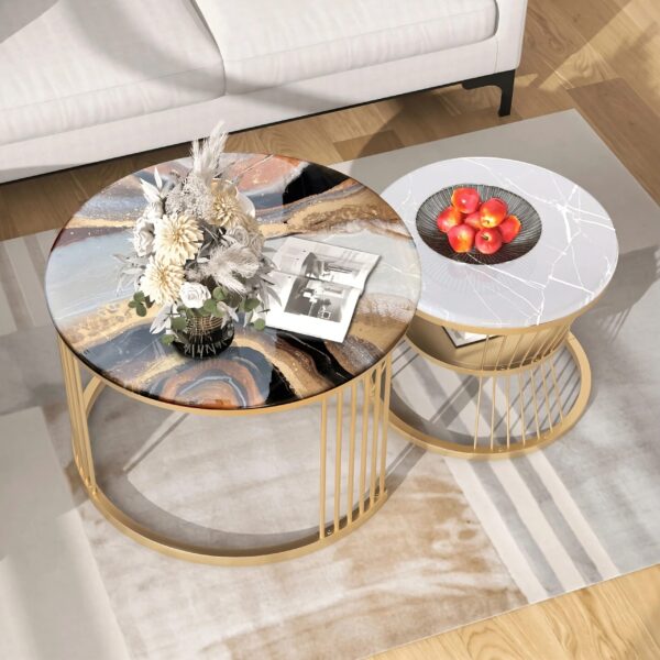 Elegant set of two round nesting coffee tables featuring luxurious tops; one showcases a detailed resin art piece with earthy and blue tones, while the other boasts a sleek white marble finish with delicate gold veining. Both are supported by slender golden frames, adding a touch of sophistication and glamour to the modern living room setup.