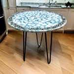 Unique round table with a top designed to resemble blue and white agate stone, set against a backdrop of a kitchen. The table features sleek black metal legs, highlighting its modern aesthetic and functional design, ideal for adding a touch of elegance and contemporary style to any interior space.