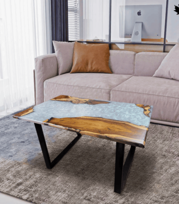 Contemporary center table featuring a unique design with a split surface; one half showcases natural wooden textures and the other half a flowing aqua blue resin that mimics water. The table is supported by sleek, black angular legs, perfectly complementing the modern and cozy living room setting with a plush taupe sectional sofa and a soft grey rug.