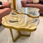 The Dual-Tone Artistic Custom Tables Table from Fankaarlok features a uniquely organic design with smooth, flowing lines and dual-tone wood, accented by embedded geode-like resin inclusions. Its luxurious gold frame complements the natural hues of the tabletop, making it a striking centerpiece for any modern living space.