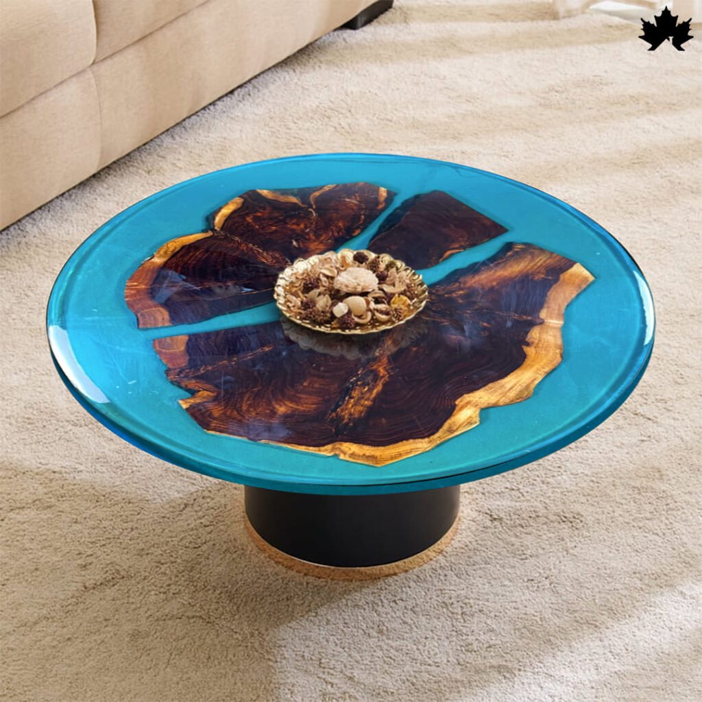 A stunning circular handcrafted resin & wood coffee table featuring a rich, wooden base with natural grain patterns. The tabletop is a vibrant blue resin that mimics a clear water body, encompassing scattered, wooden fragments, creating an illusion of islands. The resin's transparency enhances the depth and colors of the wood, making it a striking centerpiece in a cozy, carpeted living room.