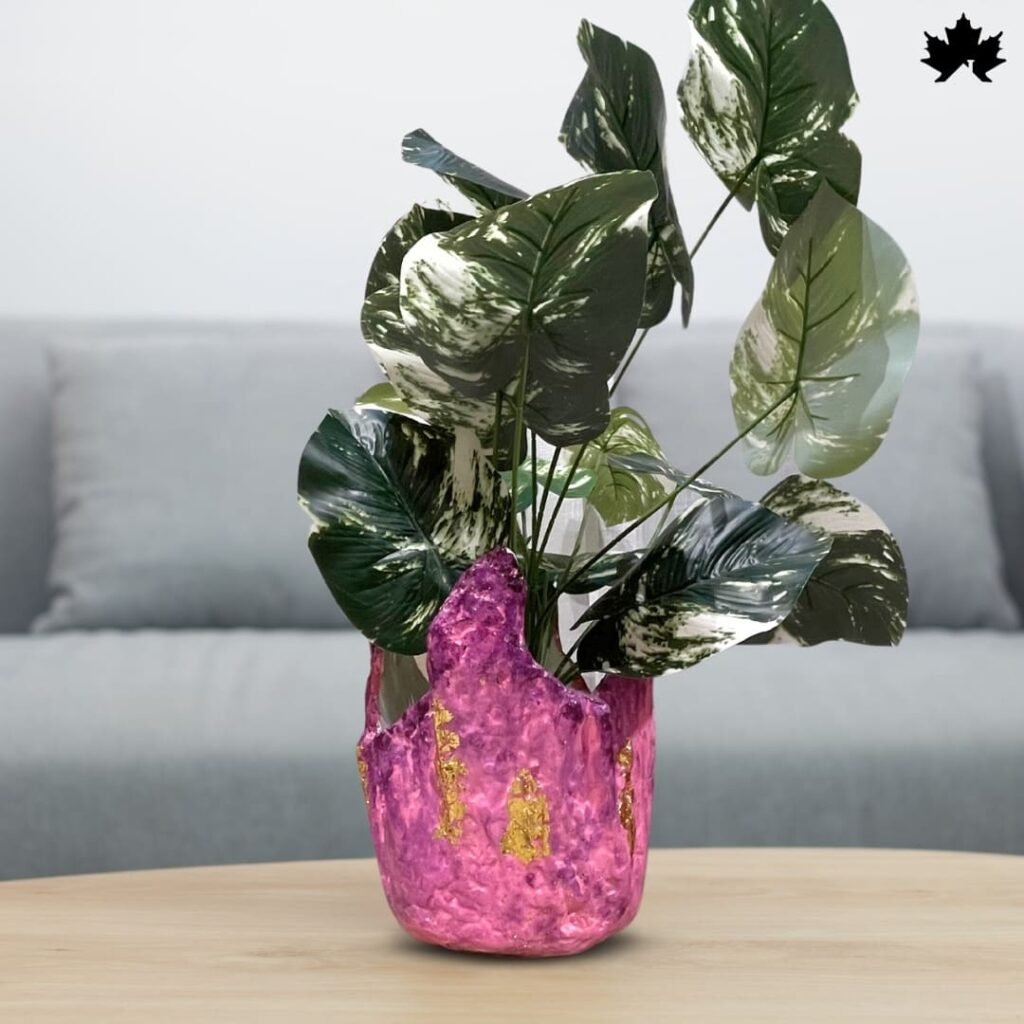 The image showcases a Blush Elegance Pink - Designer Plant Vase from Fankaarlok, featuring a textured pink resin body with gold leaf accents. This planter blends vibrant color and luxurious design, making it a striking piece for displaying plants and enhancing the decor of any modern living space.