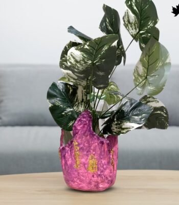 The image showcases a Blush Elegance Pink - Designer Plant Vase from Fankaarlok, featuring a textured pink resin body with gold leaf accents. This planter blends vibrant color and luxurious design, making it a striking piece for displaying plants and enhancing the decor of any modern living space.